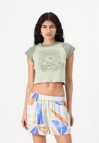 Light green cropped t-shirt with a graphic print, paired with multi-colored, patterned shorts featuring blue, orange, and pastel green accents.