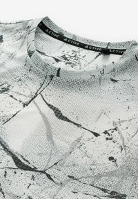 Gros plan sur le col d'un maillot de sport à motif marbré gris et noir avec étiquette de taille "M" et "Made in Portugal" imprimée à l'intérieur.