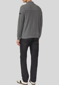 Grijze gebreide trui met een geribbelde kraag en zoom, gecombineerd met zwarte jeans en witte sneakers met een zwarte streep.