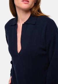 Marineblauer Strickpullover mit Kragen und tiefem V-Ausschnitt. Hat lange Ärmel und eine weiche Textur. Minimalistisches Design ohne Muster.