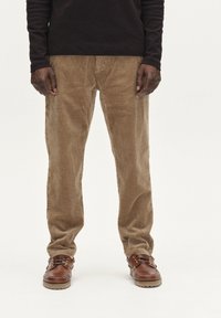 Katoenen broeken in beige met een verticale ribbelstructuur, gecombineerd met bruine veterschoenen met een ronde neus en een contrasterende zool.