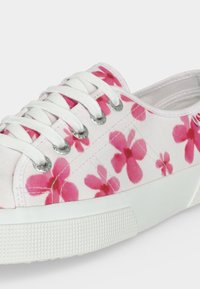 Λευκό πάνινο αθλητικό παπούτσι με ροζ σχέδιο λουλουδιών, λευκά κορδόνια, μεταλλικές οπές και υφασμένη λευκή καουτσούκ σόλα.