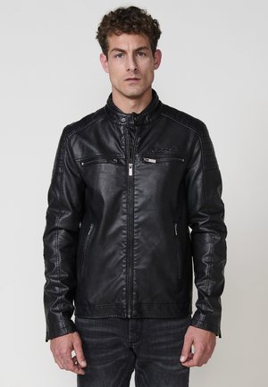 Chaqueta de moto de cuero negra con cuello alzado, cierre delantero con cremallera y dos bolsillos en el pecho con acentos de costura horizontal.