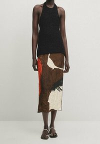 Top a halter nero e testurizzato abbinato a una gonna di lunghezza media con motivi astratti marroni, bianchi e rossi. Modella che indossa sandali piatti.