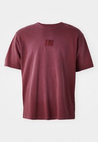 Bordeaux bomulds T-shirt med rund hals og korte ærmer, med et lille logomærke i en mørkere nuance på brystet.
