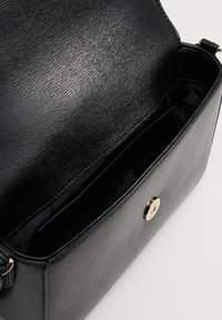 Black textured handbag with a smooth inner lining, a gold button closure, and a single adjustable strap; features multiple inner compartments.