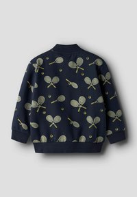 Tamsiai mėlyna bombonešio stiliaus striukė su geltonų teniso raketų ir kamuoliukų raštu, su ribotais rankogaliais ir apačia. Lygios audinio tekstūros.