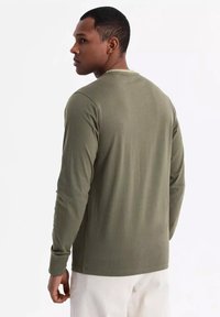 Olivgrünes Langarmshirt aus weichem Stoff mit Rundhalsausschnitt und taillierter Silhouette, nahtlosem Schultern design und minimalen Nähten.