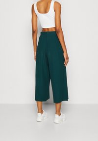Turkooizen culotte broek met een brede pijp, gestructureerde stof, hoge taille en zijsplitten. Combinatie met een strakke witte cropped top en witte sneakers.