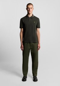 Mörkgrön polo skjorta med en kontrasterande randig krage, kombinerad med matchande gröna byxor och svarta stövlar. Enkelt, åtsittande design.