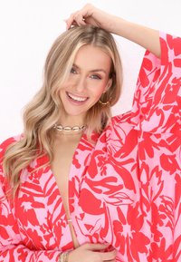 Rózsaszín és piros virágmintás kimonó, széles ujjal és mély V-nyakkivágással, könnyű anyagból készült. Réteges nyakláncokkal van kiegészítve.