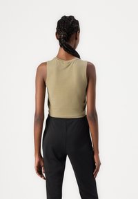 Olive green cropped tank top in a soft fabric with a round neckline and sleeveless design, paired with black high-waisted pants.