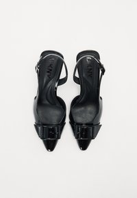 Sorte patent slingback høye hæler med spisse tær, med en spenne som aksent og teksturerte såler. Designet for et moderne og elegant utseende.