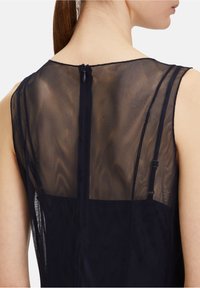 Robe navy avec un dos en maille transparente, présentant une petite fermeture éclair et de fines bretelles, mettant en valeur un tissu lisse et texturé.