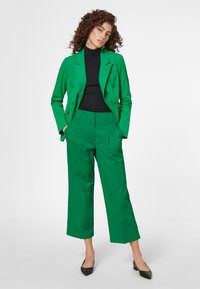 Groene dubbelbreasted blazer met een getailleerd ontwerp, gecombineerd met bijpassende cropped broek. Glad materiaal met zijzakken. Zwart top en hakken.