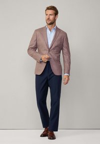 Blazer à carreaux rose clair avec revers en pointe, fermeture à un bouton, associé à une chemise bleu clair et un pantalon bleu marine. Chaussures en cuir marron.