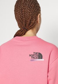 Felpa rosa realizzata in morbido cotone, con un logo nero sulla parte posteriore e una linea accentuata che recita "NON SMETTERE MAI DI ESPLORARE". Collo a costine.