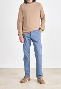 Beżowy sweter prążkowany, jasnoniebieskie spodnie i brązowe trampki. Sweter ma okrągły dekolt; spodnie mają prostą nogawkę; trampki mają niski profil.