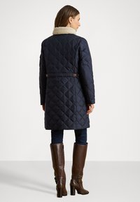 Mornarska kaputa s prešanim uzorkom i bež umjetnim krznom na ovratniku, u kombinaciji s smešnim čizmama na visoku petu i tamnoplavi trapericama.