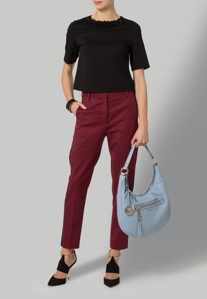 Zwarte top met korte mouwen en een geregen halslijn, bordeauxrode taillebroek, zwarte hoge hakken en een lichtblauwe schoudertas met ritsdetail.