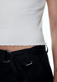 Witte geribbelde crop top met een rauwe zoom, gecombineerd met zwarte broek met een zilveren hardware riemlus en textielstof.