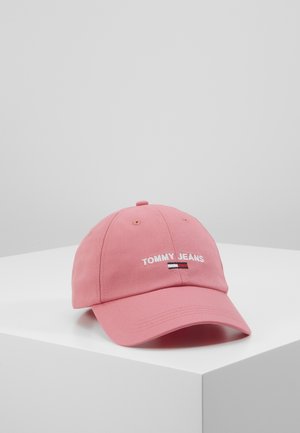 Lyserød baseballkasket med buet skygge, "Tommy Jeans" tekst og lille rød, hvid og blå flaglogo broderet midt foran på grå-hvid overflade.