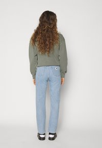 Olive green sweatshirt paired with light blue straight-leg jeans. Soft fabric; jeans have patch pocket and subtle stitching details. Black shoes with white socks.