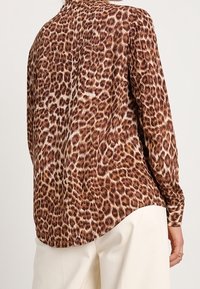 Camicia con stampa leopardata marrone, maniche lunghe, colletto a punta e orlo curvo. Realizzata in tessuto liscio con finitura lucida.
