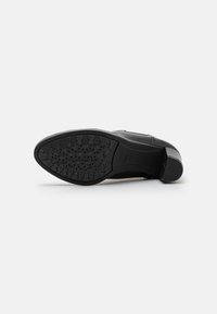 Sola de sapato de couro preto com pega de borracha texturizada, apresentando uma forma elegante e ligeiramente curva, com um padrão de sola de pequenos designs circulares e em estrela.