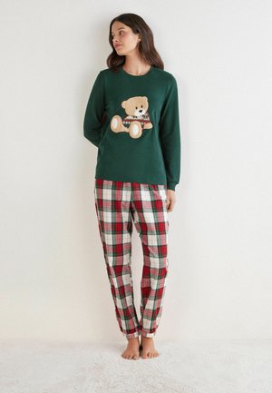 Zielona bluzka z długim rękawem z aplikacją w postaci misia, zestawiona z spodniami w czerwono-białą kratę z zielonymi i czarnymi akcentami. Materiał bawełniany.