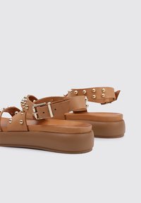 Sandalias de plataforma de tacón bajo, fabricadas con material suave, que cuentan con remaches en tono dorado, correa con hebilla y una suela contorneada para mayor comodidad.