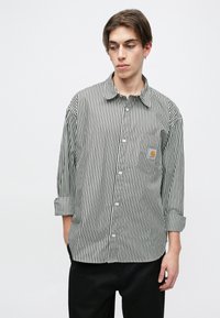 Camisa de botones a rayas blancas y negras con un bolsillo en el pecho y las mangas remangadas. Fabricada con un tejido ligero y con un corte relajado.