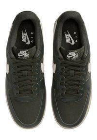 Mörkgröna sneakers med ett slätt överdel av läder och tyg, utrustade med vit branding och snören, samt en grå gummisula.