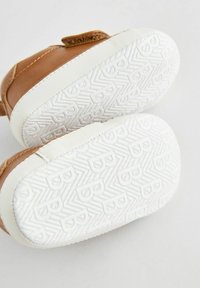 Scarpa in pelle marrone con suola in gomma bianca, caratterizzata da un motivo a zigzag testurizzato, chiusura con strap in Velcro e punta arrotondata.