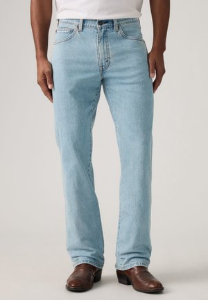 Jeans in denim azzurro chiaro con vestibilità a gamba dritta, tessuto lavato chiaro, design a cinque tasche e chiusura con bottone in metallo. Indossati con stivali marroni.