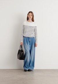 Witte en marineblauwe gestreepte langemouwen top gecombineerd met lichtblauwe wijdpijpsjeans. Zwarte handtas met korte handvatten complementeert de outfit.