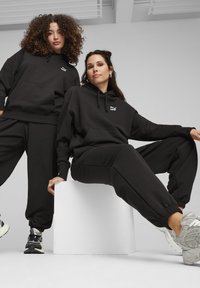 Felpe con cappuccio nere e pantaloni jogger realizzati in morbido materiale, con un piccolo logo bianco sul petto, dotati di polsini e cintura elasticizzati.