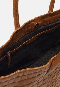 Sac fourre-tout en simili cuir beige avec texture reptile en relief, doté d'une poche zippée intérieure et d'une doublure en tissu noir avec un motif logo.