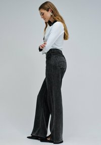 Czarne szerokie dżinsy z wysokim stanem, z lekko wyblakłą teksturą i subtelnymi detalami szycia. W połączeniu z białą bluzką z długim rękawem.