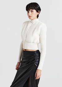 Top in finta pelliccia bianca corta con maniche a coste e colletto alto abbinato a una gonna in pelle nera con arricciature e uno spacco laterale.