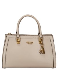 Sac à main beige GUESS avec deux poignées, quincaillerie dorée, plaque avec le nom de la marque et pendentifs décoratifs dorés et beiges à l'avant.