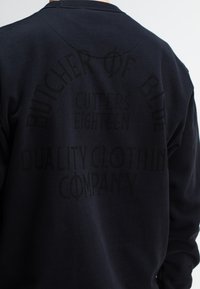 Zwarte sweatshirt van een katoenmix, met verhoogde tekstgraphics in een vervaagde zwarte tint op de achterkant. Ronde halslijn en een relaxte pasvorm.