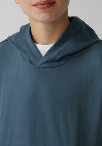Tamno plava dukserica s mekanom teksturom, koja ima visok ovratnik i opušten kroj. Tkanina izgleda glatko s minimalnim detaljima šavova.