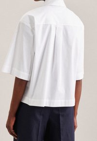 Vit kortärmad skjorta i mjukt tyg, med hög krage, avslappnad passform och en subtil yoke-söm bak.