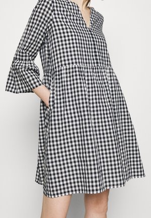 Černobílé šaty s kostkovaným vzorem gingham, výstřihem do V, tříčtvrtečními rukávy, nařaseným pasem a kapsami. Látka působí lehce a texturovaně.