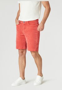 Korallfärgade kordshorts med rak skärning, som har sidofickor och knappstängning. Matchas med vita sneakers.