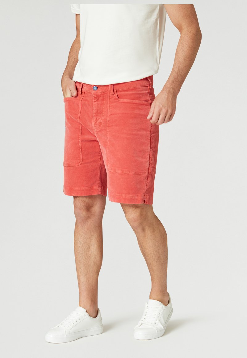 Korallfärgade kordshorts med rak skärning, som har sidofickor och knappstängning. Matchas med vita sneakers.