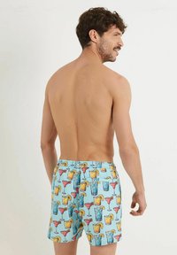 Shorts de bain pour hommes en tissu bleu clair avec des illustrations colorées de boissons répétées. Taille élastique sans poches visibles.