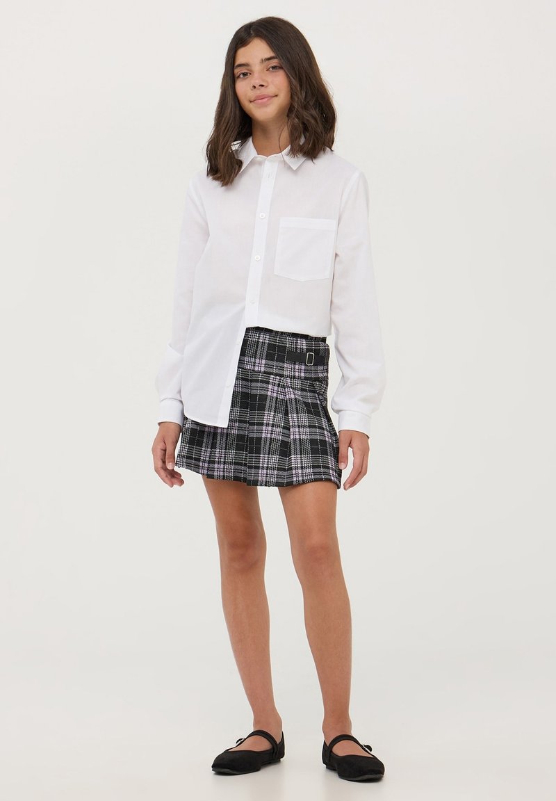 Camicia bianca con bottoni e tasca, abbinata a una gonna a pieghe a quadri nera e viola, completata da ballerine nere.