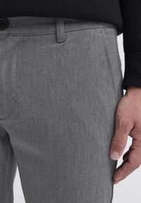 Hallitatud hallid püksid, mis on valmistatud tekstuuriga kangast, ning millel on sirge esiosa, küljetaskud ja nööbiga kinnitamine vöökoha juures.